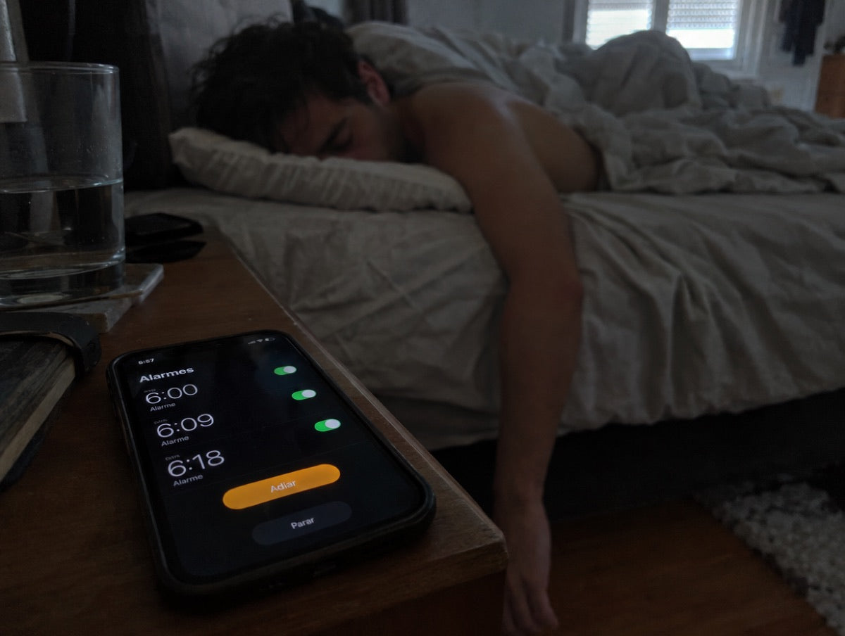 O telemóvel a tocar com três alarmes, 6:00, 6:09 e 6:18, e ele a dormir de barriga para baixo.